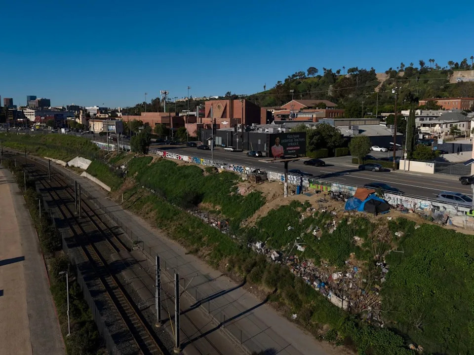 Homeless encampments and debris on a grassy hillside next to a railway and a road in Los Angeles. Andy Johnstone for California Post