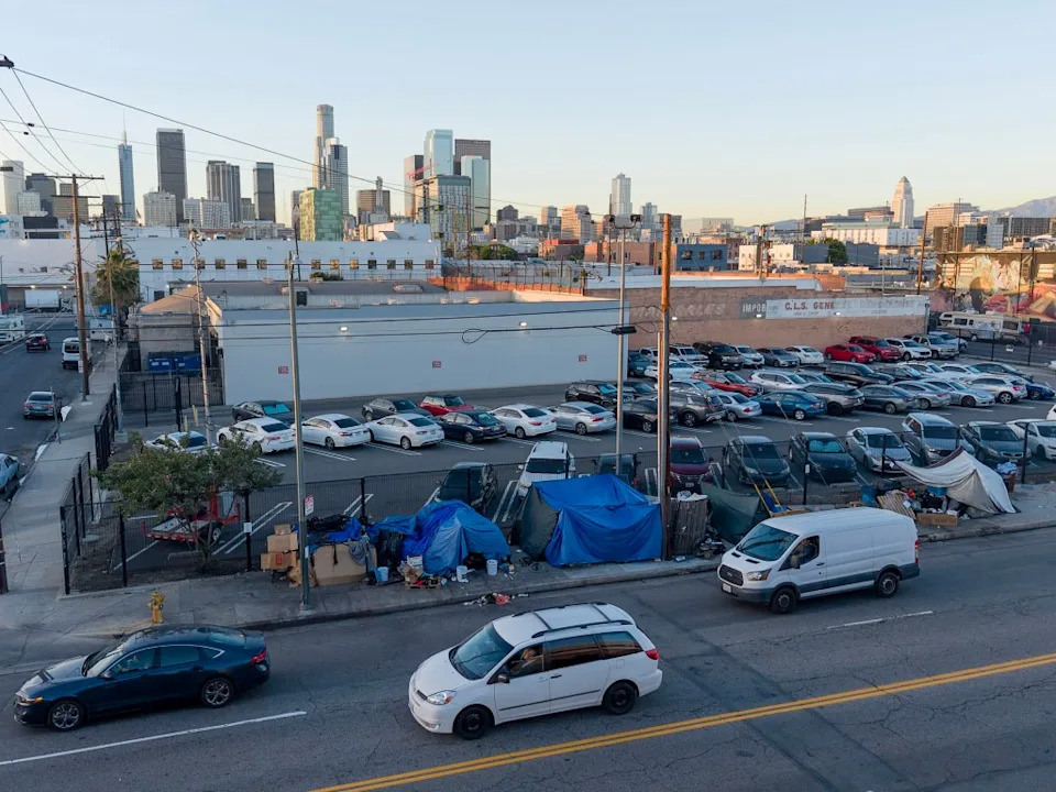 Homeless encampments line a street in Downtown Los Angeles with a city skyline in the background. Andy Johnstone for California Post