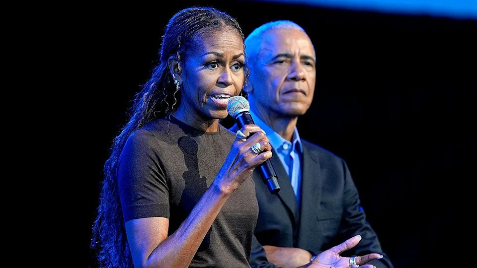 Michelle Obama speaks as Barack Obama listens at presidential center event.