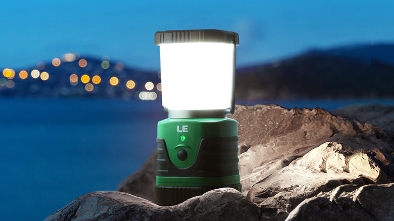 The Lepro Super Bright LED camping lantern turned on and placed on rocks outdoors.