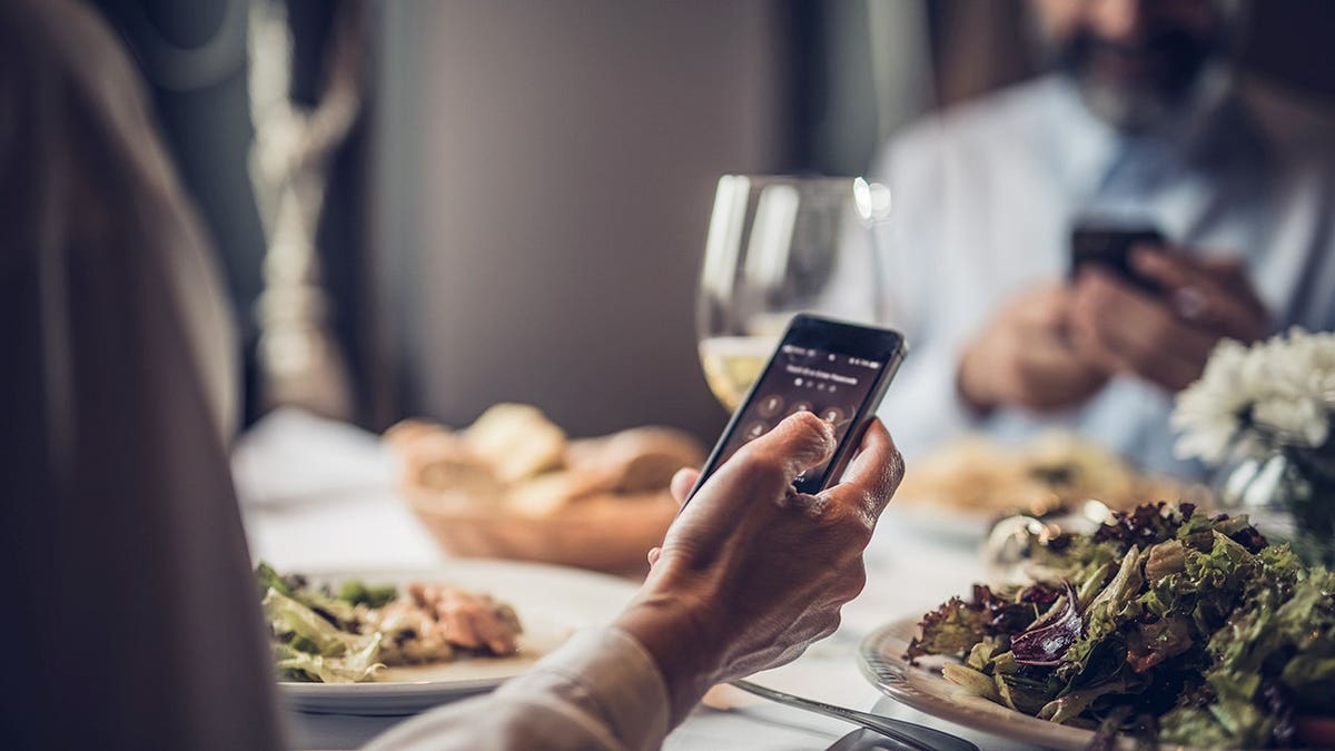 Woman entering PIN on cell phone at restaurant table.