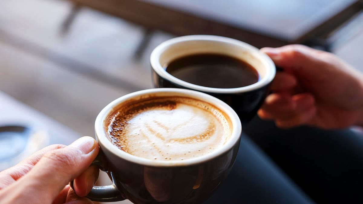 Two people clink cups of coffee together.