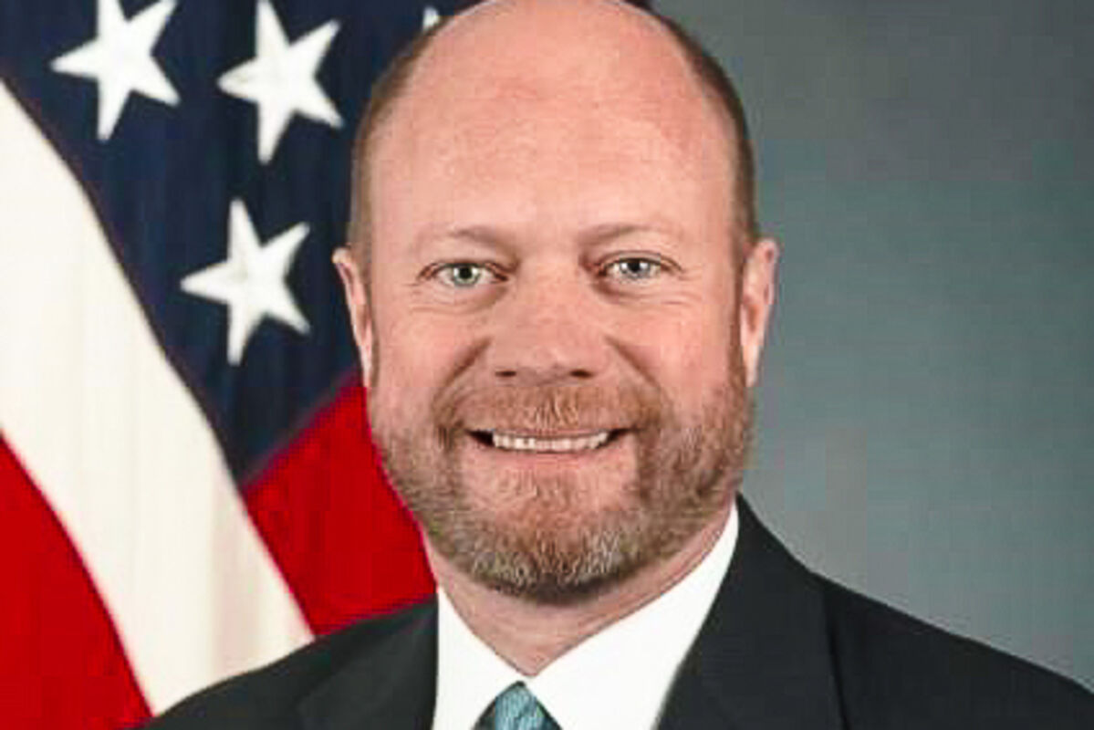 Head%20and%20shoulders%20photo%20of%20Brett%20Lambert%20in%20front%20of%20an%20American%20flag%2E