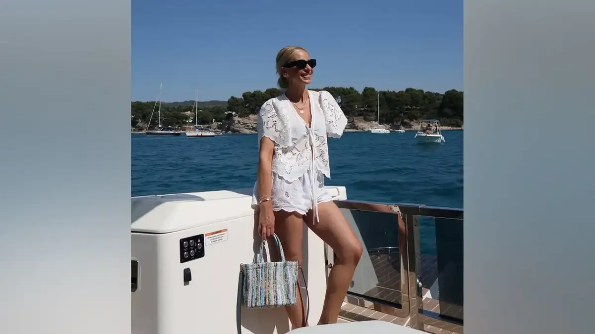 Sarah Michelle Gellar poses aboard a boat wearing a white eyelet button-up shirt and matching shorts with sunglasses and a woven tote bag during her South of France vacation.