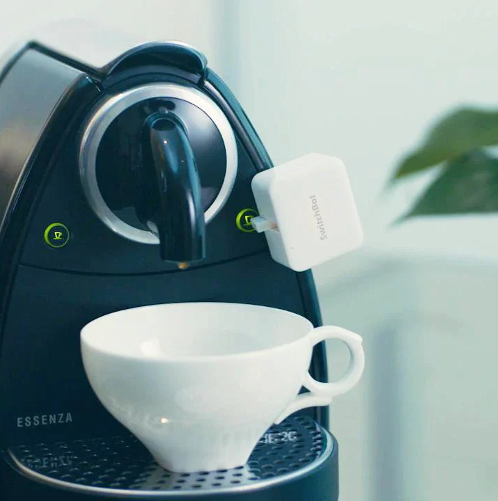 A coffeemaker with the SwitchBot button pusher attached.