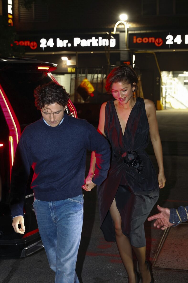 Tom Holland and Zendaya hold hands while walking together. Zendaya is in a black Ellie Saab dress.