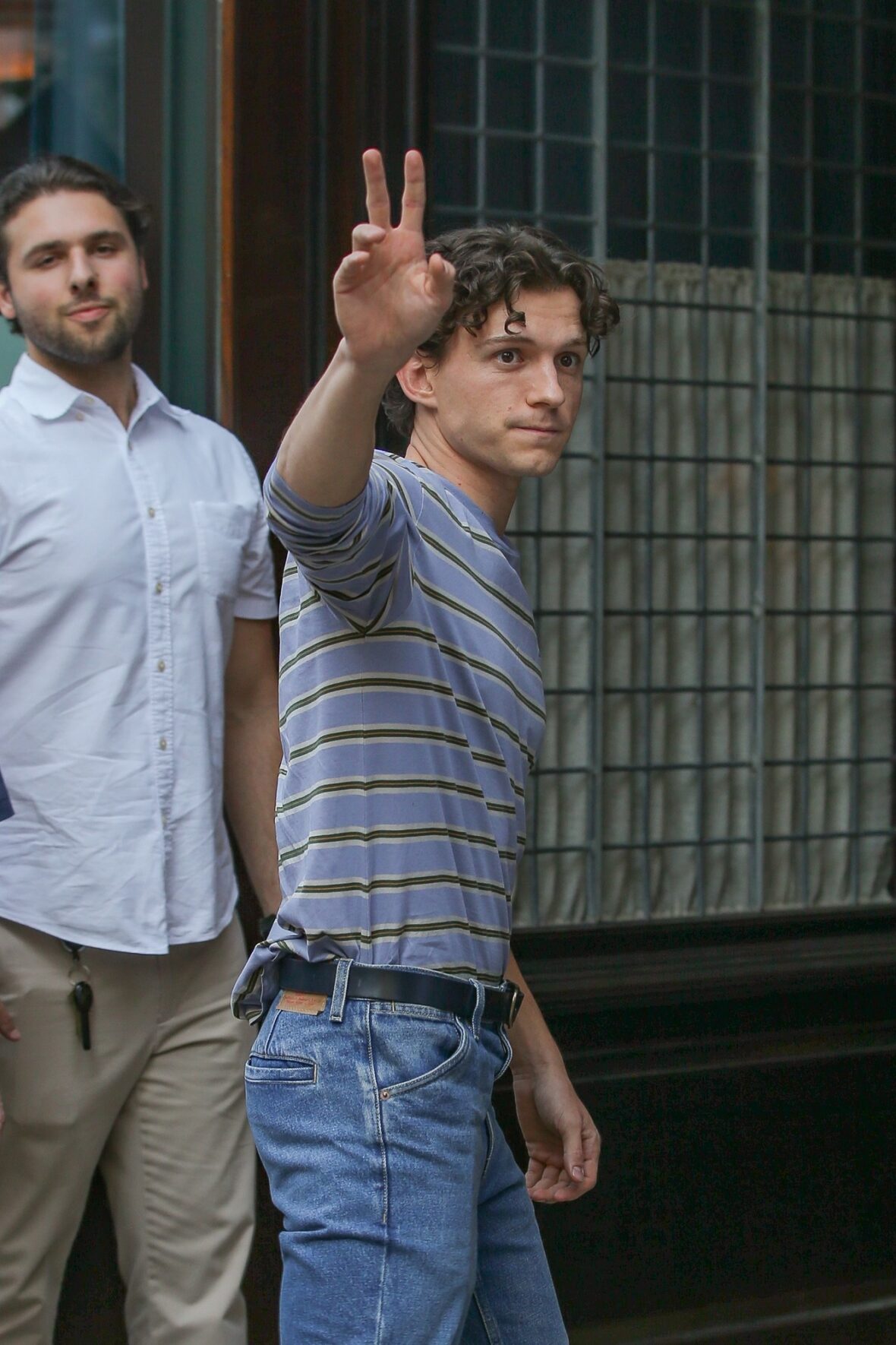 Tom Holland in a stripe long-sleeve top and jeans, holding up the peace sign.