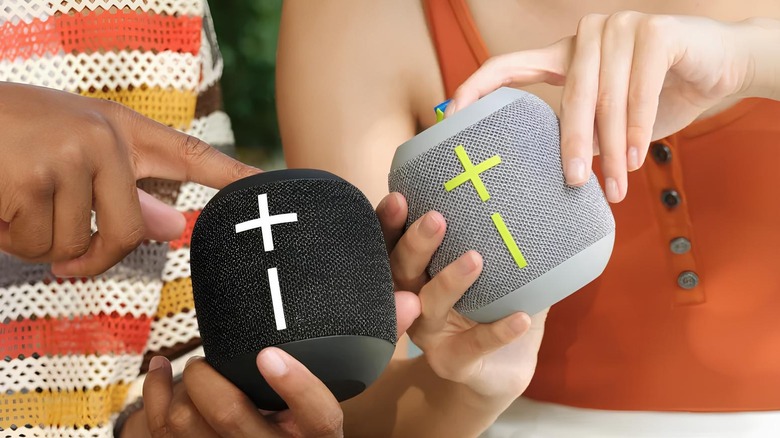 Two people holding two Wonderboom 4 speakers one black and one silver in color