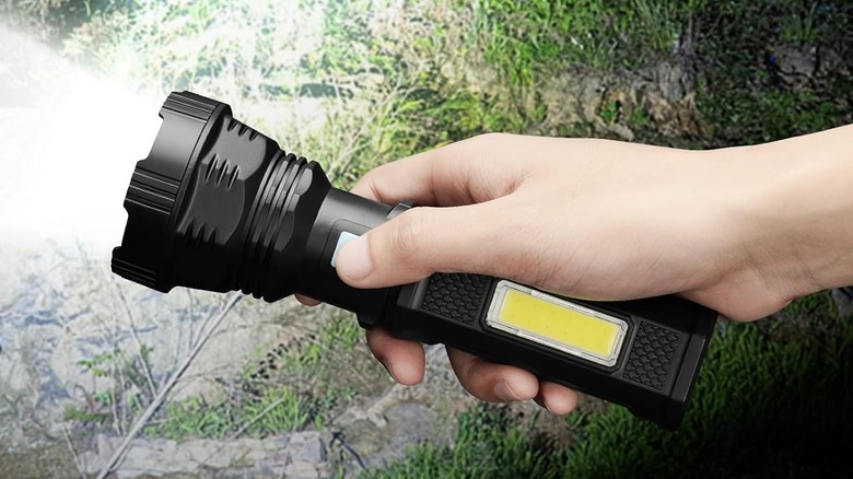 Close up of a black flashlight with a yellow panel lighting the outdoors