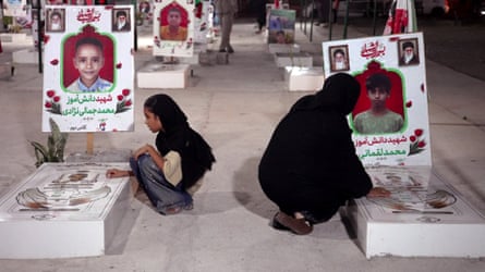 Woman and child in cemetery, large pictures of deceased children above the graves.