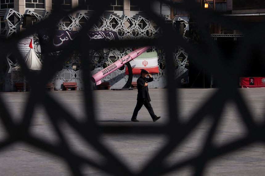 A man walks next to a symbolic mockup of an Iranian missile and an Iranian flag at Imam Hussein Square in Tehran, Iran, on July 12, 2026.