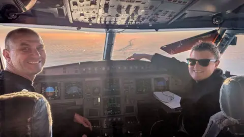 Supplied: Louise Robertson A man and a woman sit in the cockpit of a plane with the dashboard visible and snow stretching out on the Earth through the window