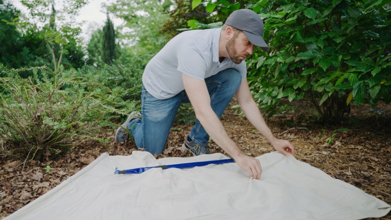 Ross Boyce collects ticks outside on a large square white blanket