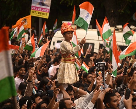 A child in traditional dress holds an Indian flag aloft above a large crowd waving flags