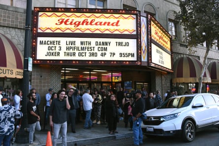 A crowd gathers beneath the marquee of a  street-side theater.