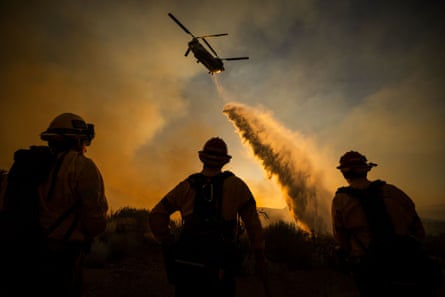 A helicopter drops water while firefighters look on
