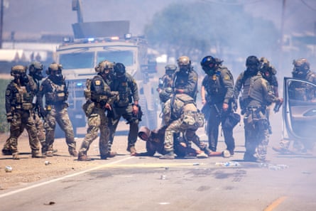 a man surrounded by officers in tactical gear is pinned to the ground