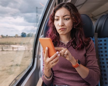 An annoyed looking woman looks at her mobile on a train.