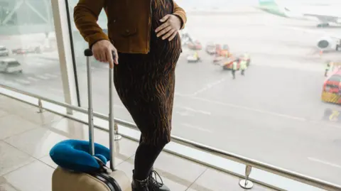 Getty Images stock image of a pregnant woman with suitcase at an airport
