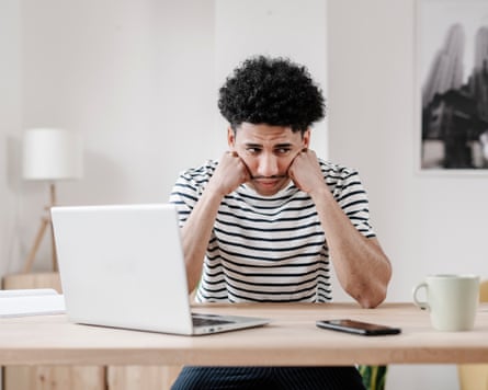 A frustrated young man at home in front of his laptop.