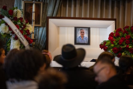 people sit in front of an open casket during a public vigil and rosary