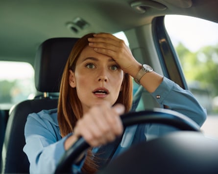 A woman holds her hand on her forehead while driving a car.