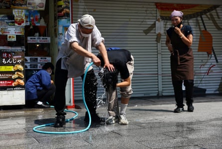 A fast-food shop worker tries to cool down a person by pouring water over his head, along Nakamise Street in Tokyo.
