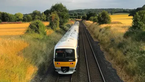 Chiltern Railways A photo of a train going through a field, there is a train in the middle on the tracks. It is a Chiltern train and you can see it's white on the top and yellow at the front.