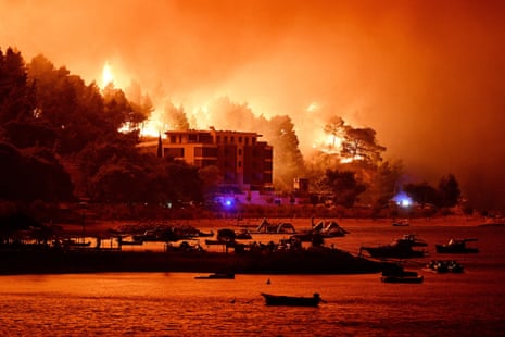 Wildfire near Omis, Croatia, blazes on a hillside at night, with boats moored on water below