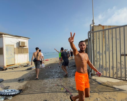 A man in orange shorts makes a V sign near an open gate