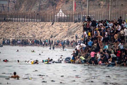 People swim in the sea on their return to Morocco from Ceuta as others stand tightly packed on an outcrop of shore