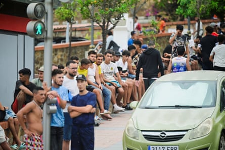People stand by a traffic light while others sit on a wall on the side of a road