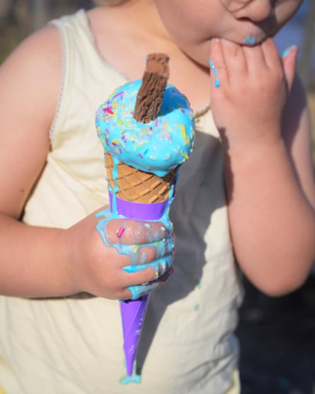 Close-up of a child eating a blue ice-cream with a chocolate flake in it, sucking her fingers