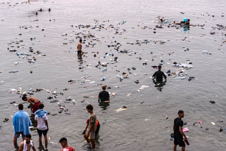 Belongings float on the surface as people stand in the shallow water