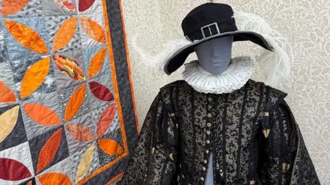 A mannequin with an ornate black and gold outfit, and a black feathered hat
