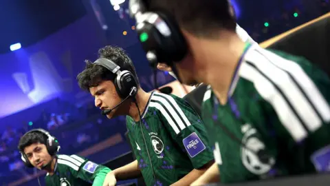 FIFA Three Esports players wearing green Saudi Arabia t-shirts in an arena, wearing black headphones with microphones on them