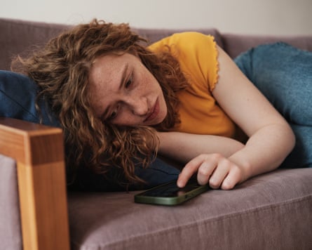 Upset redhead teen girl lying on a sofa looking at her phone.