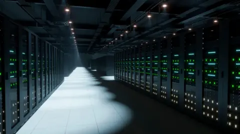 Getty Rows of computer servers with LED lights fill a dark room. The floor tiles and some of the systems are illuminated by spotlighting.