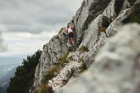 Ultrarunner Sophie Woods scales a steep alpine trail using a cable handhold above a valley