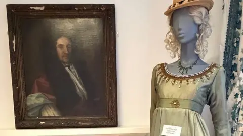 An oil painting of a man next to a mannequin of a woman with a green dress
