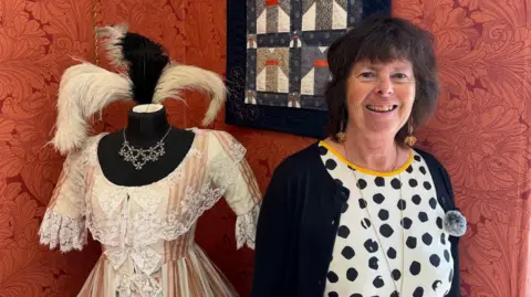 A woman with a spotted black and white top and dark hair stands next to a mannequin.