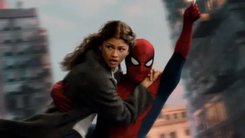 Sony Pictures/Marvel Spider-Man swings through the city on web whilst holding MJ, played by Zendaya.