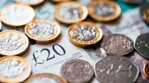 Getty Images A stock image which is a close up of British cash with notes and coins. The picture includes a £20 note and a range of coins including £1 coins, 50ps and 20ps.