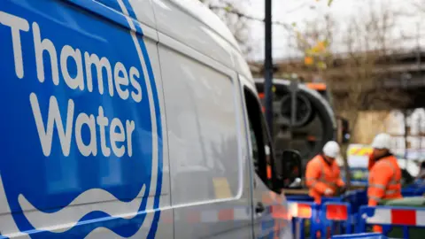 Reuters A shot of a Thames Water van. In the background there are two men wearing hi-vis clothing and hard hats and standing in an area that is boarded off by blue fences.