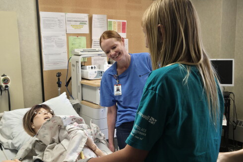 A nurse and a student work with a doll that acts as a birthing simulator