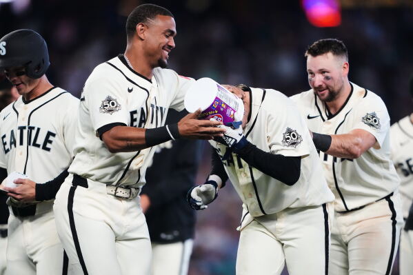 Seattle Mariners' Julio Rodríguez, left, puts a gum bucket on the head of teammate Colt Emerson as they celebrate Emerson's walk-off RBI single during the ninth inning for a win over the Minnesota Twins in a baseball game, Sunday, Aug. 2, 2026, in Seattle. (AP Photo/Lindsey Wasson)