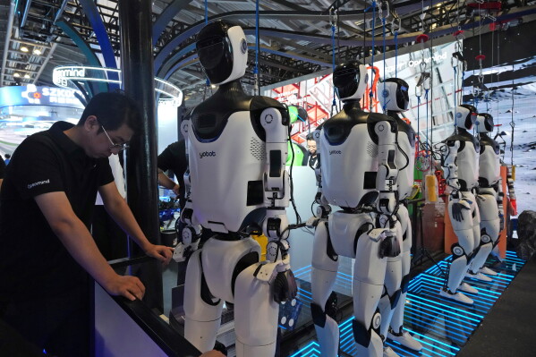 A worker reacts near a line of humanoid robots displayed at the World AI Conference in Shanghai, Friday, July 17, 2026. (AP Photo/Ng Han Guan)