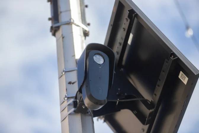 A low angle close up view of a black camera and small solar panel attached to a pole.