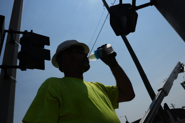 Dean Malcom drinks water while wiring street lights in extremely hot weather July 14, 2026, in Detroit. (AP Photo/Paul Sancya, File)