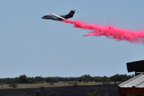 A tanker aircraft dumps fire retardant on a field southwest of Salado, Texas, Wednesday, Aug. 12, 2026, after a military helicopter crashed and sparked a grass fire. (Brent Johnson/The Killeen Daily Herald via AP)